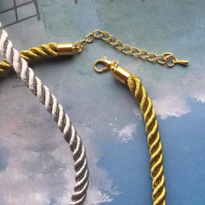 May include: Two necklaces, one silver and one gold, with a gold chain connector. The necklaces are made of braided cord.