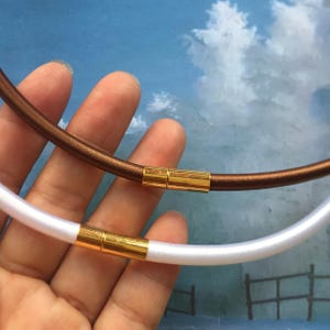 May include: Two elastic necklaces with magnetic clasps. One necklace is brown and the other is white.