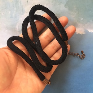 May include: A black choker necklace with a fabric cord and a copper chain. The necklace is adjustable and has a simple design.