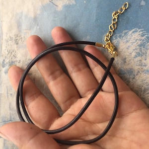 May include: A black leather cord necklace with a gold clasp.