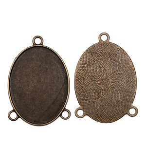 May include: Two antique gold oval-shaped metal pendant trays with three loops on each side. One tray has a smooth surface and the other has a decorative patterned surface.