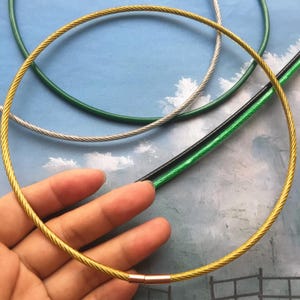 May include: A close-up of a gold cable chain necklace. The necklace is made of a thin, braided cable and has a simple, modern design. The necklace is lying on a table with other cable chains in different colours.