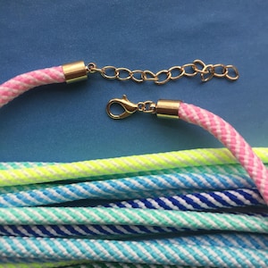 May include: A multi-colored striped rope necklace with a gold chain and clasp. The rope is made of several different colors, including pink, blue, green, and yellow.