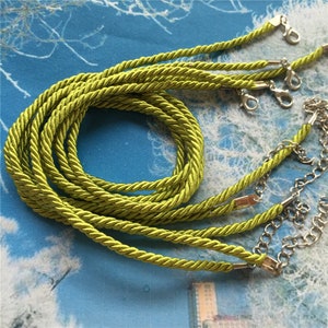 May include: A close-up of a set of lime green braided cords with silver lobster clasps. The cords are twisted together and are ready to be used for jewelry making or other crafting projects.
