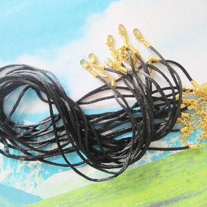 May include: A bundle of black cord necklaces with gold lobster clasps. The cords are arranged in a pile, with the clasps visible at the top.
