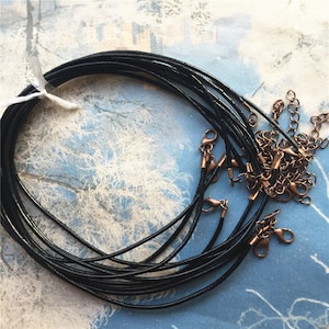 May include: A bundle of black leather cords with lobster clasps. The cords are arranged in a circle and are ready to be used for jewelry making.