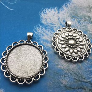 May include: Two silver pendant charms with a filigree design. One charm has a blank circular space for a cameo or photo. The other charm has a raised floral design.