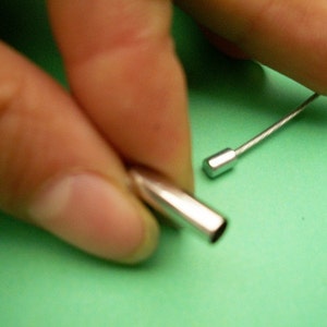 Peut inclure: Gros plan sur deux embouts de c&acirc;ble de couleur argent. Une extr&eacute;mit&eacute; est tenue dans une main, tandis que l'autre extr&eacute;mit&eacute; est pos&eacute;e sur une surface verte.