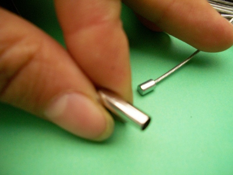 Peut inclure: Gros plan sur deux embouts de c&acirc;ble de couleur argent. Une extr&eacute;mit&eacute; est tenue dans une main, tandis que l'autre extr&eacute;mit&eacute; est pos&eacute;e sur une surface verte.