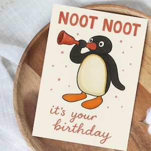 Puede incluir: Tarjeta de felicitación de cumpleaños con una ilustración de un pingüino de dibujos animados. El pingüino es blanco y negro con pies naranjas y una trompeta roja. El texto "NOOT NOOT" está en la parte superior y "it's your birthday" en la inferior.