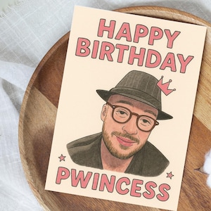 May include: A birthday card with a portrait of a man wearing glasses and a hat, with the words "HAPPY BIRTHDAY" and "PWINCESS" in pink letters. The card has a light beige background and is decorated with stars.