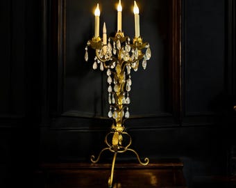 May include: A gold candelabra with three lit candles and crystal accents. The candelabra has a decorative, ornate design and sits on a dark wooden surface.