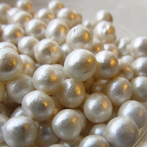 May include: A bowl filled with white pearl-like candy sprinkles. The sprinkles are round and have a slightly iridescent sheen.