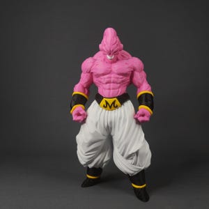 Può includere: Action figure rosa di un personaggio muscoloso con testa a punta, pantaloni bianchi e stivali neri. La figura ha una cintura nera con fibbia dorata "M" e bracciali neri con finiture gialle. La figura è su sfondo grigio.