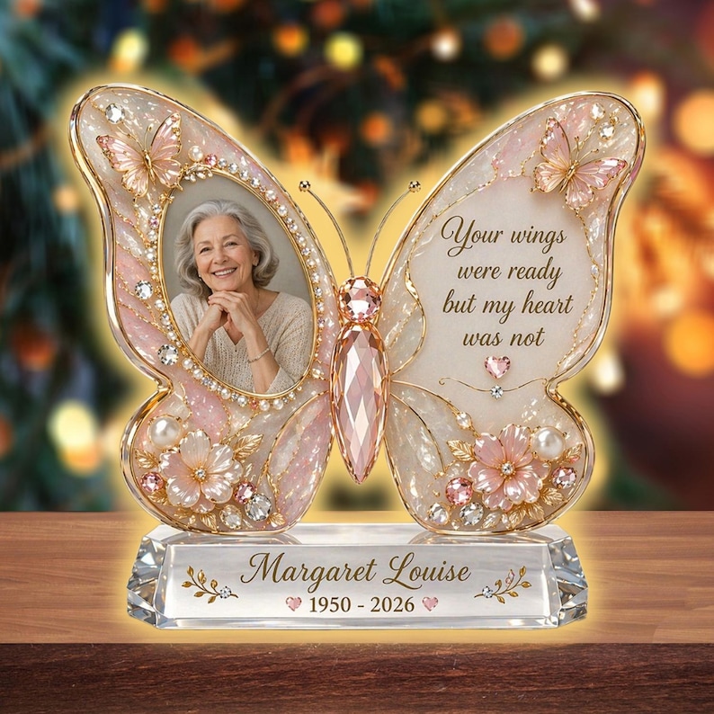 May include: A butterfly-shaped memorial photo frame with a photo of a woman. The frame is decorated with pink and white accents, crystals, and pearls. Text reads "Your wings were ready but my heart was not" and "Margaret Louise 1950-2026".