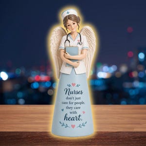 May include: A figurine of a nurse angel, wearing a white uniform with a stethoscope and holding a blue notepad. The angel has feathered wings and a light blue skirt with the text "Nurses don't just care for people, they care with heart."