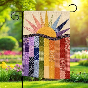 May include: A rectangular garden flag featuring a quilted design of a rising sun with multi-colored fabric rays in pink, yellow, green, blue, and purple. The lower section consists of vertical fabric strips in a rainbow of colors and patterns.