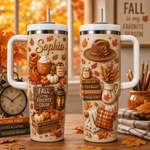 May include: Two beige tumblers with handles and straws, decorated with 3D-style autumn motifs. The left tumbler features the name Sophia, a mug, pumpkins, and a sign reading Fall is my favourite colour. The right tumbler displays a hat, books, and a pitcher.