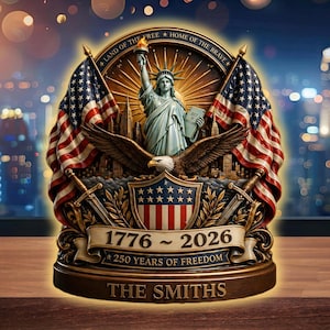 May include: A decorative emblem featuring the Statue of Liberty, American flags, and an eagle. The design includes the text "Land of the Free, Home of the Brave," "1776 ~ 2026," and "250 Years of Freedom." The base reads "The Smiths."