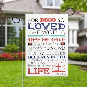 Könnte beinhalten: Eine weiße Gartenflagge mit dem Text "FOR GOD SO LOVED THE WORLD" in Rot, Blau und Schwarz. Die Flagge enthält den Bibelvers Johannes 3:16 und eine Kreuzgrafik. Die Flagge wird auf einem schwarzen Metallständer im Garten gezeigt.