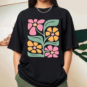 Puede incluir: Camiseta negra con estampado gráfico de flores estilizadas de color rosa, naranja y verde.