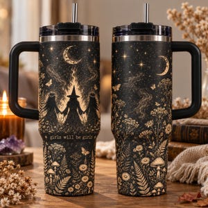 May include: Two black stainless steel tumblers with handles and straws, featuring a gold-toned celestial and botanical print. The design includes three figures, a crescent moon, stars, butterflies, ferns, mushrooms, and the text "girls will be girls."
