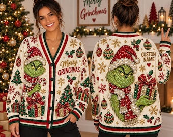 Könnte beinhalten: Eine cremefarbene V-Ausschnitt-Strickjacke mit einem grünen Grinch-Motiv, roten und grünen Weihnachtskugeln, Tannenbäumen und Schneeflocken. Die Vorderseite zeigt den Text Merry GRINCHMAS, die Rückseite den Text CUSTOM NAME.