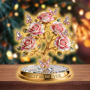 May include: A decorative golden tree sculpture with pink roses and crystal butterflies. The base reads "BEST MOM EVER". The roses have crystal accents, and the butterflies have names on them. The sculpture sits on a mirrored surface.