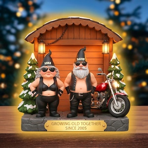 Può includere: Statuetta di una coppia di gnomi motociclisti con occhiali da sole, gilet di pelle e pantaloni neri, in piedi davanti a una capanna di legno. Una moto rossa è parcheggiata accanto. La base recita "GROWING OLD TOGETHER SINCE 2005."