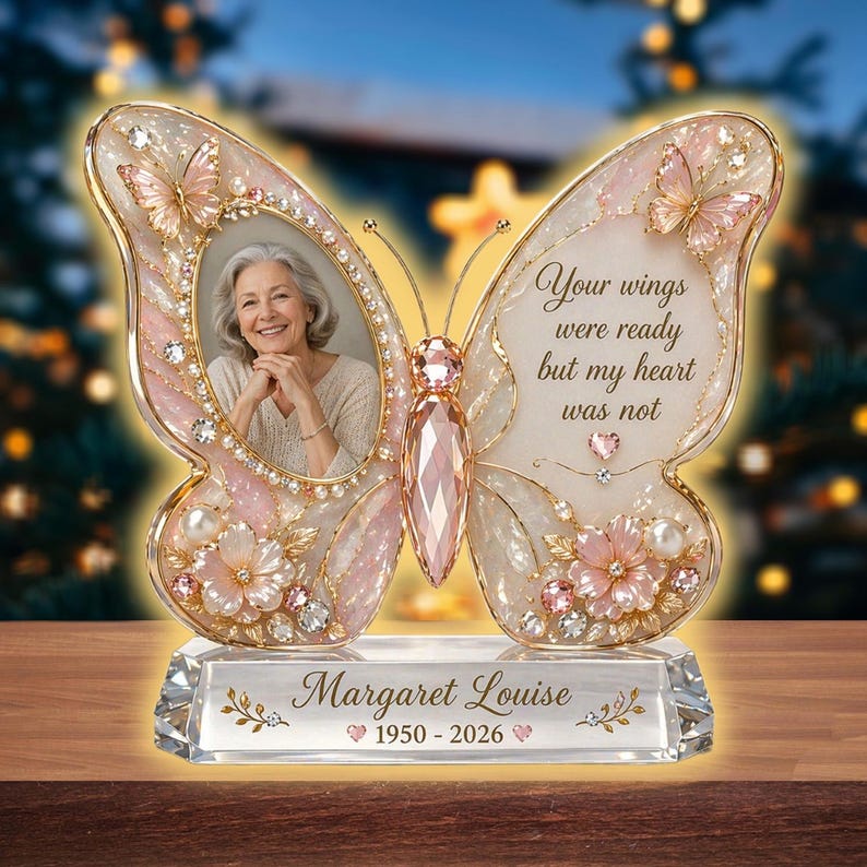 May include: A butterfly-shaped memorial photo frame with a picture of a woman. The frame is decorated with pink and white accents, butterflies, and floral details. Text on the frame reads "Your wings were ready but my heart was not" and "Margaret Louise 1950-2026".