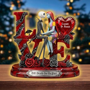 Puede incluir: Una escultura decorativa roja y negra con Jack Skellington y Sally de The Nightmare Before Christmas, sentados en las letras "LOVE". Se incluye una gema en forma de corazón con los nombres "Lucas & Anna". La base dice "Till Death Do Us Part".