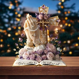 May include: A religious figurine featuring praying hands, a cross, and roses. The cross is adorned with purple gems and gold accents. The base is an open book with the text "God is within her, She will not fall".