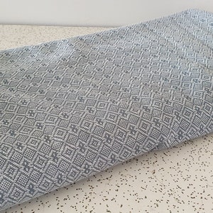 May include: A light blue woven fabric with a white diamond pattern. The fabric is folded in half and lying on a white surface.