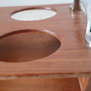 Op de afbeelding: Houten dienblad met zes ronde uitsparingen en een metalen handvat. Het dienblad is bruin en het handvat is zilverkleurig.