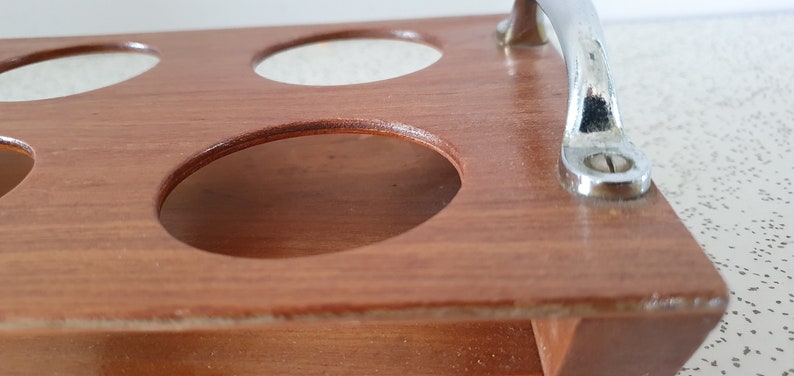 Op de afbeelding: Houten dienblad met zes ronde uitsparingen en een metalen handvat. Het dienblad is bruin en het handvat is zilverkleurig.