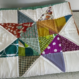 May include: A white quilt with a star design made from various colourful fabric scraps. The star is made from green, purple, red, yellow, and blue fabric.