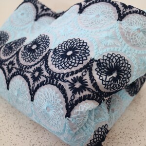 May include: A light blue fabric with a delicate floral pattern embroidered in black thread. The fabric is folded in half, showing the intricate details of the design.