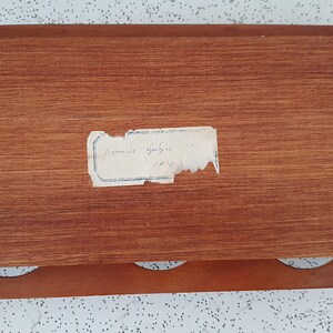 Op de afbeelding: Een houten doos met drie gaten aan de voorkant en een label met de tekst "Samuel Appleton 1745".