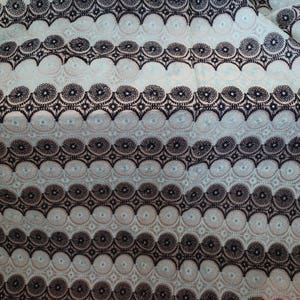 May include: A close-up of a light blue fabric with a black and white geometric pattern. The pattern is made up of circles and stars.