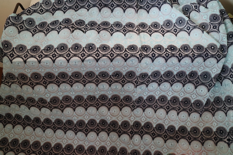 May include: A close-up of a light blue fabric with a black and white geometric pattern. The pattern is made up of circles and stars.