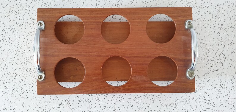 Op de afbeelding: Een houten dienblad met zes ronde uitsparingen en twee metalen handvatten. Het dienblad is gemaakt van lichtbruin hout en heeft een natuurlijke afwerking. De handvatten zijn zilverkleurig en hebben een gepolijste afwerking.