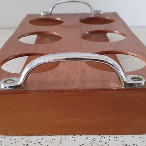 Op de afbeelding: Een houten dienblad met zes ronde uitsparingen en twee metalen handvatten. Het dienblad is bruin en de handvatten zijn zilverkleurig.
