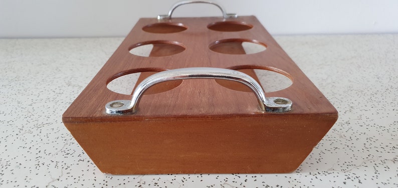 Op de afbeelding: Een houten dienblad met zes ronde uitsparingen en twee metalen handvatten. Het dienblad is bruin en de handvatten zijn zilverkleurig.