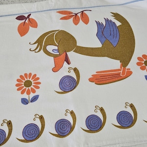 May include: White fabric with a repeating pattern of cartoon ducks, snails, and flowers in shades of brown, orange, and blue. The ducks have blue wings and orange feet and beaks. The flowers are orange and brown.