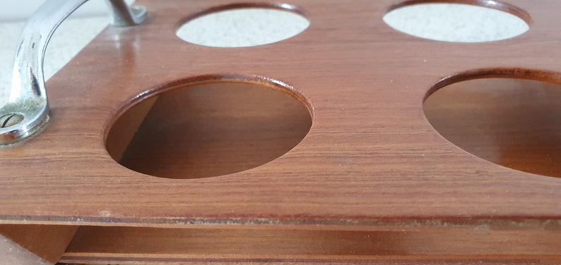 Op de afbeelding: Houten serveerblad met een chromen handvat en zes ronde uitsparingen. Het blad is gemaakt van lichtbruin hout met een gladde afwerking.