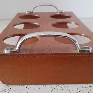 Op de afbeelding: Een houten dienblad met zes ronde uitsparingen en twee metalen handvatten. Het dienblad is bruin en de handvatten zijn zilverkleurig.