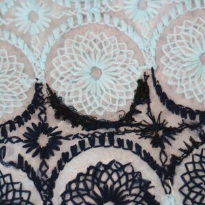 May include: A close-up of a sheer fabric with blue and black embroidered floral patterns. The fabric has a delicate, lacy texture.