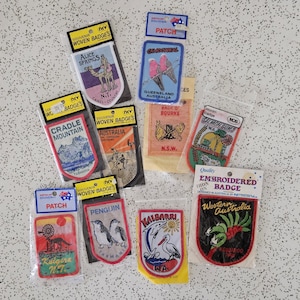 May include: A collection of ten rectangular and shield-shaped souvenir woven and embroidered patches in individual plastic packaging. Each patch features colourful illustrations of Australian landmarks, wildlife, and locations with text labels.