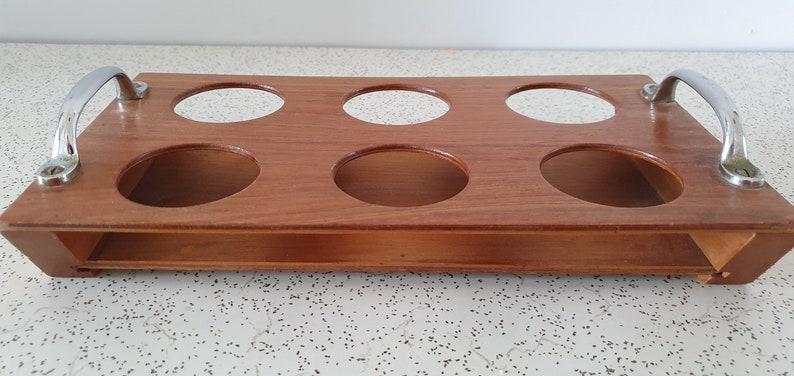 Op de afbeelding: Houten dienblad met zes ronde uitsparingen en twee metalen handvatten. Het dienblad is bruin en heeft een natuurlijke houten afwerking.