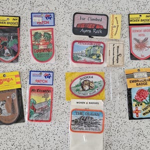 May include: A collection of ten rectangular and shield-shaped souvenir woven and embroidered patches featuring various Australian locations and landmarks, including Margaret River, Darwin, Ayers Rock, Peterborough, Glendambo, Mt. Ebenezer, Quokka, and New South Wales.